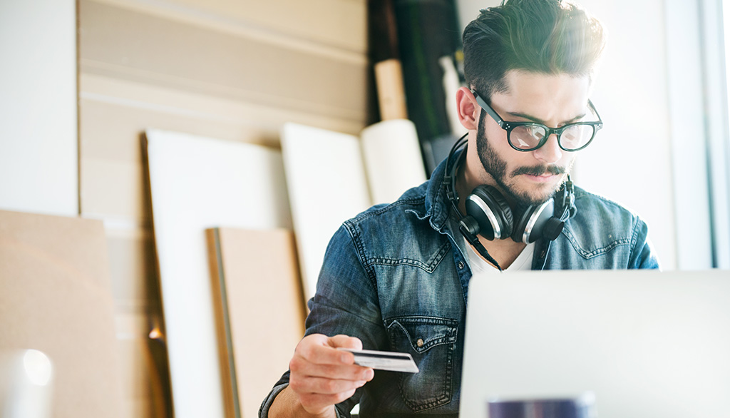 Man holding a credit card and looking at a laptop